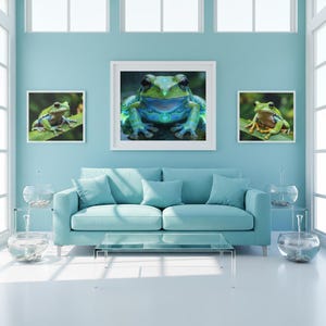 Peut inclure: Un salon avec un canapé bleu clair, une table basse en verre et trois impressions d'art de grenouilles encadrées. L'art représente une grenouille verte avec des accents bleus et verts. La pièce a un mur bleu clair et des boiseries blanches.