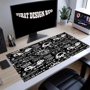 Puede incluir: Alfombrilla de escritorio para juegos en blanco y negro con un patrón repetido de mandos, auriculares y texto. La alfombrilla tiene las palabras "VIDEO GAMES" y "ESCAPE GAME" en un estilo manuscrito. El texto "TURAT DESIGN RUG" está en la pantalla del ordenador.