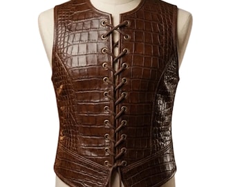 May include: A brown leather vest with a crocodile skin texture. The vest has a lace-up front and a round neckline. The vest is sleeveless and has a tailored fit. The vest is displayed on a mannequin.