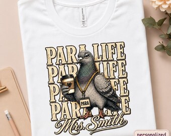 Könnte beinhalten: Ein weißes Kurzarm-T-Shirt mit einer Grafik eines Taubenvogels, der einen Kaffeebecher hält. Die Taube trägt eine goldene Kette mit einem Anhänger mit der Aufschrift PARA. Der Hintergrundtext wiederholt PARA LIFE in abgenutzter Goldoptik.