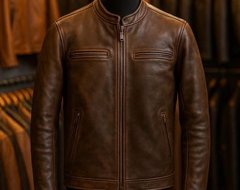 May include: A brown leather jacket with a zip-up front, two chest pockets, and two side pockets. The jacket is displayed on a black mannequin. Other leather jackets are visible in the background.