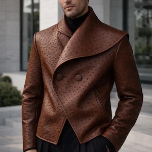 Può includere: Giacca in pelle marrone con un motivo strutturato unico e un design doppiopetto. La giacca presenta un ampio colletto e due grandi bottoni. Il modello indossa un dolcevita nero e pantaloni neri.