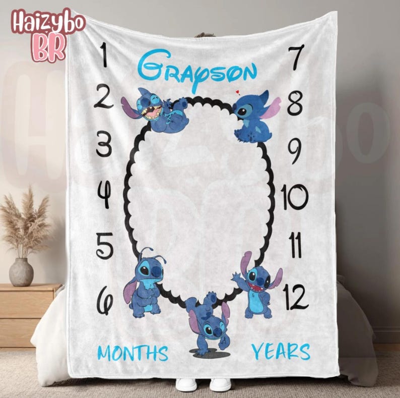 May include: A white milestone blanket featuring the name Grayson in blue script, numbers 1 through 12 in black, and four blue alien characters surrounding a central black scalloped oval frame, with the words MONTHS and YEARS printed in blue.