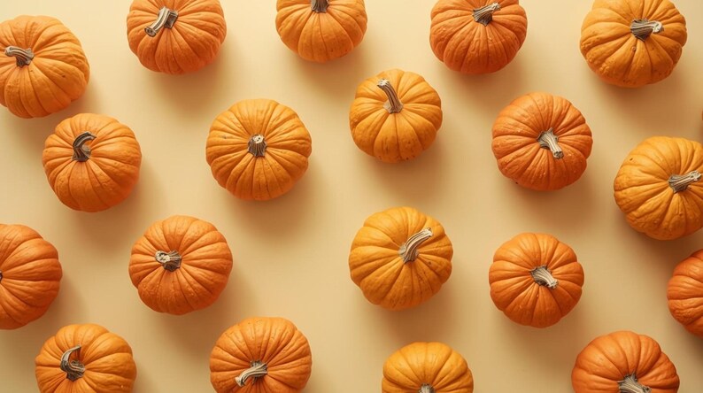 Puede incluir: Vista a&eacute;rea de un patr&oacute;n de peque&ntilde;as calabazas naranjas con superficies texturizadas y tallos verde-marrones. Las calabazas est&aacute;n dispuestas sobre un fondo amarillo claro, creando un tema oto&ntilde;al.