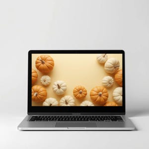 Puede incluir: Un port&aacute;til plateado muestra una imagen oto&ntilde;al. La pantalla presenta un fondo amarillo claro adornado con calabazas naranjas y blancas. Las calabazas son de diferentes tama&ntilde;os y est&aacute;n dispuestas alrededor de la pantalla.