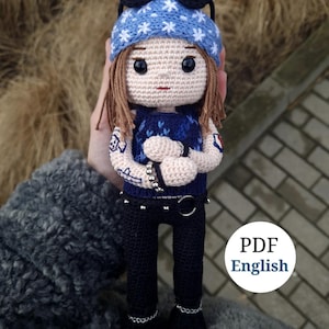 May include: A handmade crochet doll with brown hair, wearing a blue hat with white stars, a blue vest, black pants, and black boots. The doll has tattoos on its arms and is holding its arms crossed. The doll is wearing a silver chain belt. The image includes the text "PDF English".