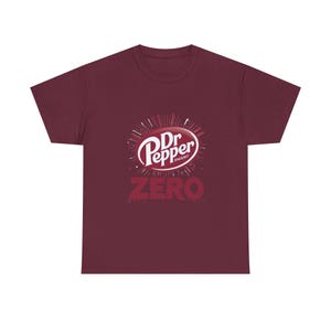 Może przedstawiać: Bordowa koszulka z logo Dr Pepper w kolorze białym i czerwonym oraz napisem "ZERO" w kolorze czerwonym poniżej. Koszulka ma okrągły dekolt i krótkie rękawy.