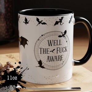 May include: White ceramic mug with a black interior and handle. The mug features a design of black dragons and the text "WELL THE FUCK AWARE" in a circular design. The mug is 11oz.