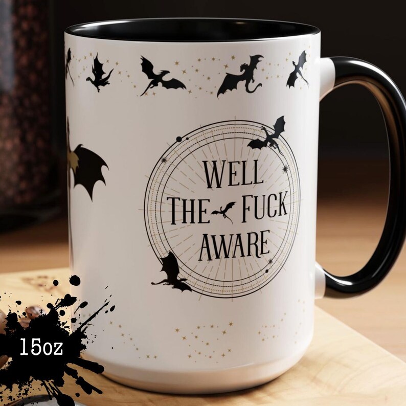 May include: A white ceramic mug with a black handle and rim. The mug features a design of black bats and the text "WELL THE FUCK AWARE" in a circular design. The mug holds 15oz.