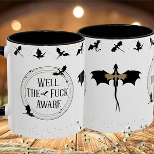 May include: White ceramic mug with a black interior and handle. The mug features a dragon design and the text "WELL THE FUCK AWARE" in a circular frame. Black dragon silhouettes are scattered around the mug.