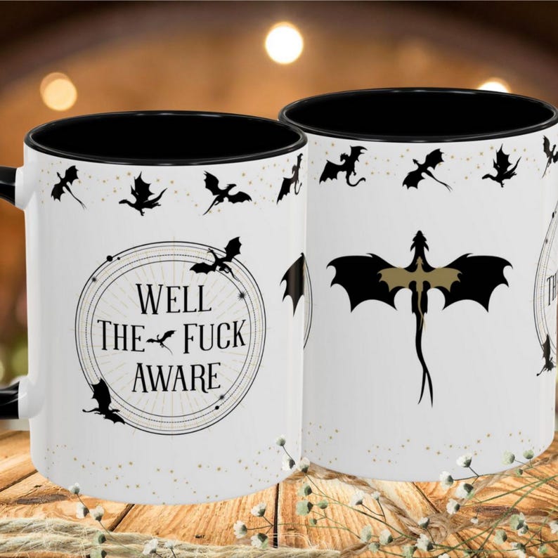 May include: White ceramic mug with a black interior and handle. The mug features a dragon design and the text "WELL THE FUCK AWARE" in a circular frame. Black dragon silhouettes are scattered around the mug.