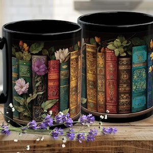 May include: Two black ceramic mugs with a colorful design of vintage books and flowers. The books are in various colors, including green, red, and blue, with floral accents. Lavender sprigs are in the foreground. A decorative item for a book lover.