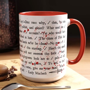 May include: White ceramic mug with a red interior and handle. The mug features text from Shakespeare's Macbeth, with red blood splatter accents and a dagger illustration. The quote is attributed to Lady Macbeth.