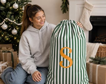 May include: A large fabric drawstring sack featuring a vertical dark green and white striped pattern. The front of the sack is personalized with a large, bold, orange-colored capital letter S centered in the middle of the striped design.
