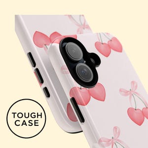 May include: White phone case featuring a pattern of pink cherries and bows. The case has a black camera lens and the text "TOUGH CASE" in a black circle.