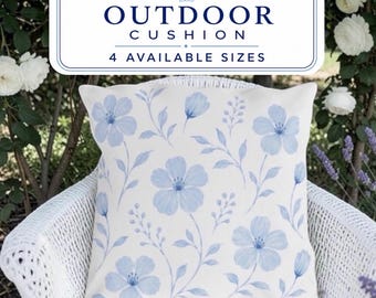 May include: A square outdoor cushion featuring a light cream background with a repeating pattern of soft blue watercolor-style flowers and delicate stems. The text OUTDOOR CUSHION 4 AVAILABLE SIZES is displayed in a white box above the cushion.