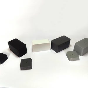 Peut inclure: Une collection de blocs rectangulaires et carrés en noir, blanc et gris. L'ensemble comprend quatre blocs rectangulaires plus hauts et trois blocs carrés plus courts, chacun présentant une finition lisse et un petit trou circulaire sur le dessus.