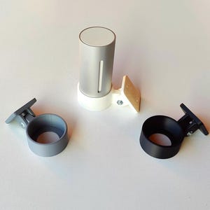 Peut inclure: Un objet cylindrique argenté et blanc avec une rainure verticale, monté sur une base blanche et un support en bois. Deux supports circulaires, un gris et un noir, sont également présents, chacun avec un support de montage.