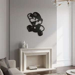 K&ouml;nnte beinhalten: Schwarze Metall-Wandkunst, die die Figur Mario in einer Laufpose darstellt. Das Kunstwerk ist an einer hellgrauen Wand &uuml;ber einem Kamin angebracht. Der Raum hat eine neutrale Farbpalette mit einer modernen &Auml;sthetik.