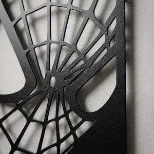 May include: A matte black metal wall art piece featuring a laser-cut spider web design. The geometric pattern consists of thin, intersecting lines radiating from a central point, creating a series of open, irregular quadrilateral shapes.