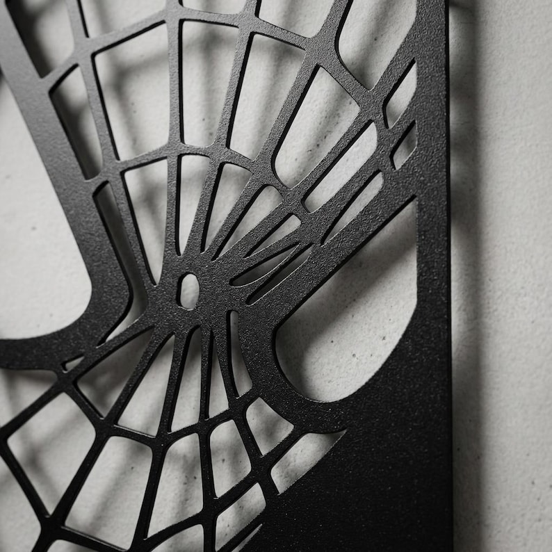May include: A matte black metal wall art piece featuring a laser-cut spider web design. The geometric pattern consists of thin, intersecting lines radiating from a central point, creating a series of open, irregular quadrilateral shapes.