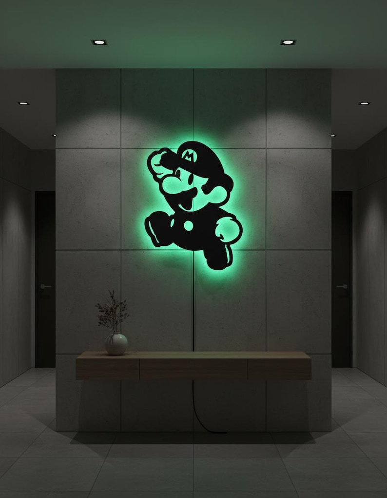 K&ouml;nnte beinhalten: Eine schwarze Silhouette der Videospiel-Figur Mario in Laufpose, beleuchtet mit gr&uuml;nem Leuchten. Das Kunstwerk ist an einer grauen gefliesten Wand in einem Flur angebracht. Unterhalb befindet sich eine Holzkonsolentisch mit einer Vase.
