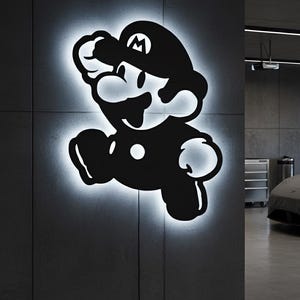 K&ouml;nnte beinhalten: Schwarz-wei&szlig;e, beleuchtete Wandkunst mit einer Silhouette der Videospiel-Figur Mario in einer Sprungpose. Das Kunstwerk ist an einer grauen Wand angebracht und strahlt ein sanftes, wei&szlig;es Leuchten um die Konturen der Figur aus.
