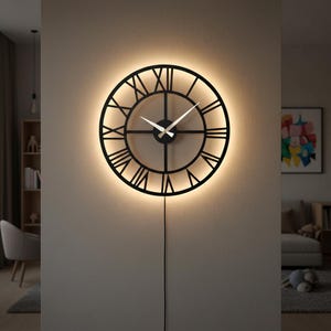 Op de afbeelding: Een zwarte, ronde wandklok met Romeinse cijfers en een warme gloed. De wijzers van de klok zijn wit en een zwart netsnoer hangt naar beneden. De klok is bevestigd aan een neutraal gekleurde muur.