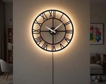 May include: A black, circular wall clock featuring Roman numerals and a warm, illuminated glow. The clock hands are white, and a black power cable hangs down. The clock is mounted on a neutral wall.