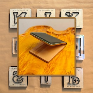 May include: A leather wallet with a green top and tan interior is displayed on a wooden surface. Surrounding the wallet are various wooden stamps with metal designs and text. The stamps have the text "LXJ25123122G" and other numbers.