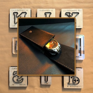 May include: A black leather watch case containing a gold-toned watch with a black strap. The watch face is gold. Wooden blocks with metal shapes and text, such as "LXJ25123122G 14" and "ZM02-60", surround the case.