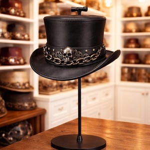 May include: A black top hat with a decorative chain, skull, and gear accents. The hat is displayed on a black stand. The hat is a steampunk style accessory.