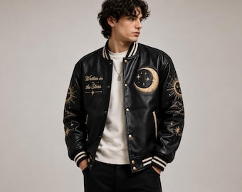May include: A black varsity jacket featuring gold embroidered celestial motifs including a crescent moon, sun, and stars. The text "Written in the Stars" is embroidered on the chest. The jacket has a snap-button front and striped ribbed cuffs and collar.