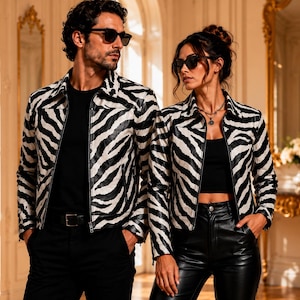 May include: Two individuals wearing matching black and white zebra-striped jackets. The jackets feature a collared neckline, long sleeves, and a front zip fastening. Both individuals are wearing dark sunglasses and solid black shirts underneath.