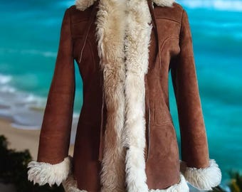 May include: A brown coat featuring a thick cream-colored faux fur trim along the collar, front opening, and sleeve cuffs. The garment has long sleeves and a structured fit, with visible seams running vertically down the front panels.