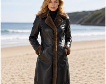 May include: A black leather coat with brown fur trim on the collar, cuffs, and down the front. The coat is knee-length and has pockets. The person is standing on a sandy beach with the ocean in the background.