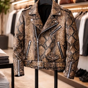 Op de afbeelding: Bruin en zwart leren jack met slangenpatroon in klassieke bikerstijl. Voorzien van een reverskraag, meerdere zakken met ritssluiting en een riem in de taille. De jas wordt gepresenteerd op een zwarte hanger in een winkel.