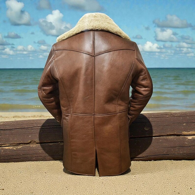 May include: A brown leather jacket featuring a thick cream-colored shearling collar. The jacket has a paneled construction with visible seams, long sleeves, and a straight hemline with a center back vent, presented from a rear view.
