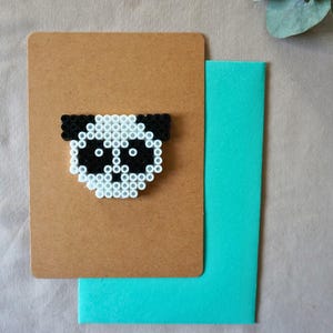 Peut inclure: Une carte de vœux faite à la main avec un motif de panda réalisé avec des perles noires et blanches. Le panda est fixé à une carte marron, avec une enveloppe turquoise en dessous. Parfait pour envoyer un message spécial.