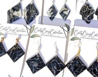 May include: A collection of handmade earrings with various shapes and designs. The earrings feature a marbled black and white pattern. Some have silver hooks, while others have gold-colored posts. The cards read "Caits Clay Collection" and "caitsclaycollection.etsy.com".