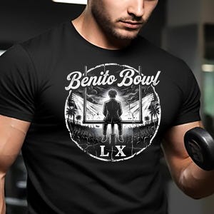 May include: Black t-shirt with a circular graphic featuring the text "Benito Bowl" and a silhouette of a person in a stadium setting. The shirt is being worn while lifting a dumbbell in a gym setting.