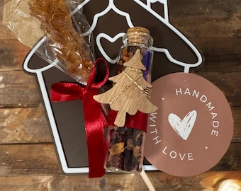May include: A gift set featuring a brown house-shaped cutout with a red ribbon, a glass vial filled with tea, a wooden Christmas tree, and a wrapped candy stick. A round tag reads "HANDMADE WITH LOVE."