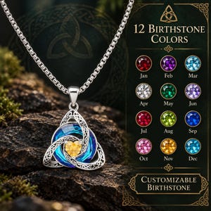 May include: A silver-toned necklace featuring a triquetra pendant with an intricate Celtic knot design. The pendant holds a circular blue crystal and a central yellow heart-shaped stone. A chart displays 12 birthstone colors with labels.