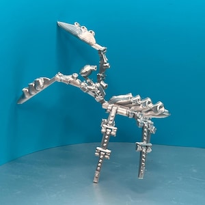 May include: A silver-coloured, articulated, 3D printed model of a creature with a long neck, a tail, and four legs. The model is posed in a standing position with its head tilted to the side.