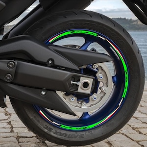 Può includere: Ruota di moto con pneumatico nero e cerchio blu. Il cerchio presenta un design a strisce verdi, bianche e rosse con la scritta "SCORPION". Lo pneumatico è montato su un telaio nero della moto.