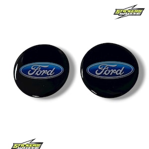 Puede incluir: Dos pegatinas negras y brillantes con el emblema de Ford. Cada pegatina circular presenta el logotipo de Ford en un óvalo azul con texto blanco. Las pegatinas están sobre un fondo blanco. El texto "STICKERS WHITE" está en la esquina superior derecha.