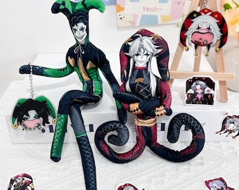 May include: Two plush jester dolls with long limbs and pointed hats, one in green and black and one in red and black. The set includes several acrylic keychains and stickers featuring illustrated jester characters with white hair and expressive faces.