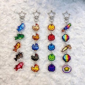 May include: Four vertical keychains featuring pixel art charms attached to silver star-shaped clasps. The charms depict various colorful fish, chickens, fruits, and geometric shapes in a retro 8-bit style, arranged in a linear vertical sequence.