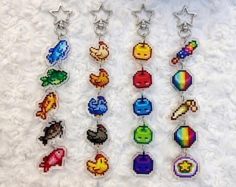 May include: Four vertical keychains featuring pixel art charms attached to silver star-shaped clasps. The charms depict various colorful fish, chickens, fruits, and geometric shapes in a retro 8-bit style, arranged in a linear vertical sequence.