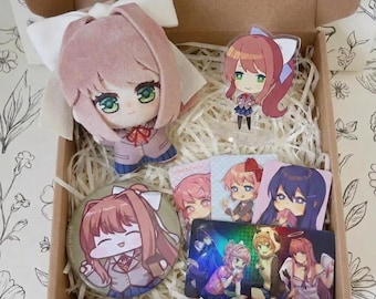 May include: A gift box containing a plush doll with pink hair and a white bow, an acrylic standee of a character with a ponytail, a circular pinback button, three square cards, and a rectangular card featuring multiple anime-style characters.